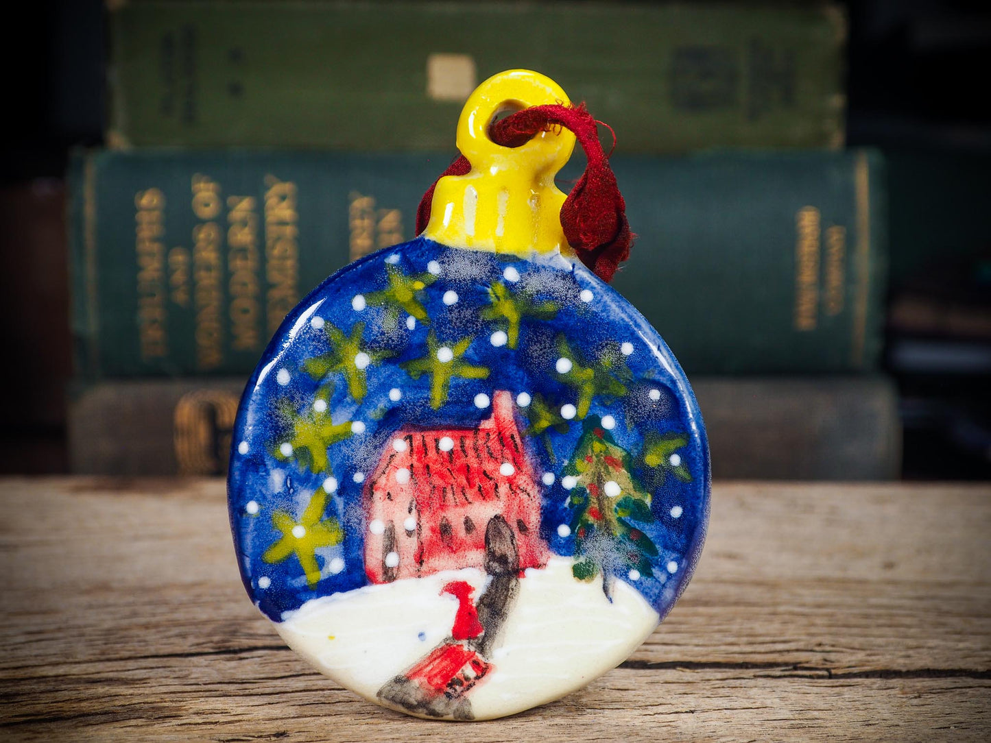 Handmade ceramic winter night ornament with red house, snowy scene, and painted stars, created by Idania Salcido aka Danita Art for Christmas decorating or gifting.