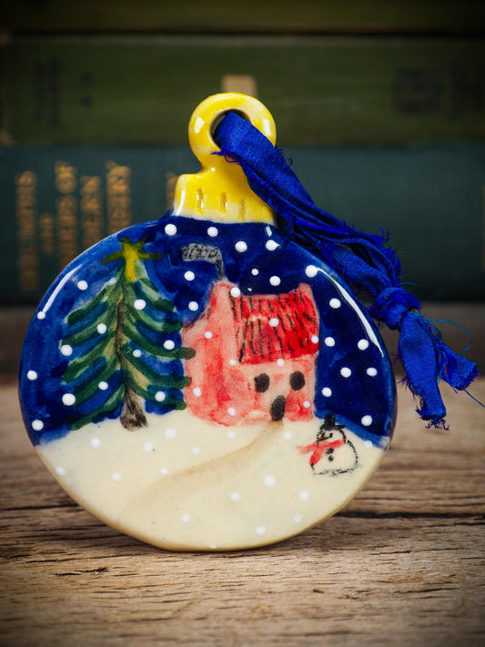 Handmade ceramic winter cottage ornament with snowman and tree, created by Idania Salcido aka Danita Art for Christmas decorating or gifting.