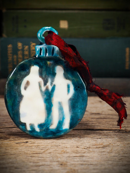Handmade ceramic ornament with ethereal couple silhouettes and blue-green background, created by Idania Salcido aka Danita Art.