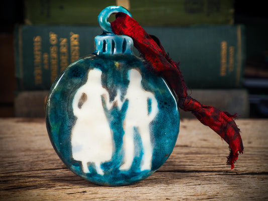 Handmade ceramic ornament with ethereal couple silhouettes and blue-green background, created by Idania Salcido aka Danita Art.