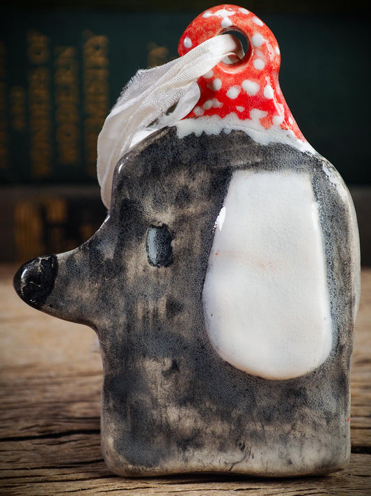 Handmade ceramic dog ornament with gray coat, white ear, and red dotted hood, created by Idania Salcido aka Danita Art for Christmas decorating or gifting.