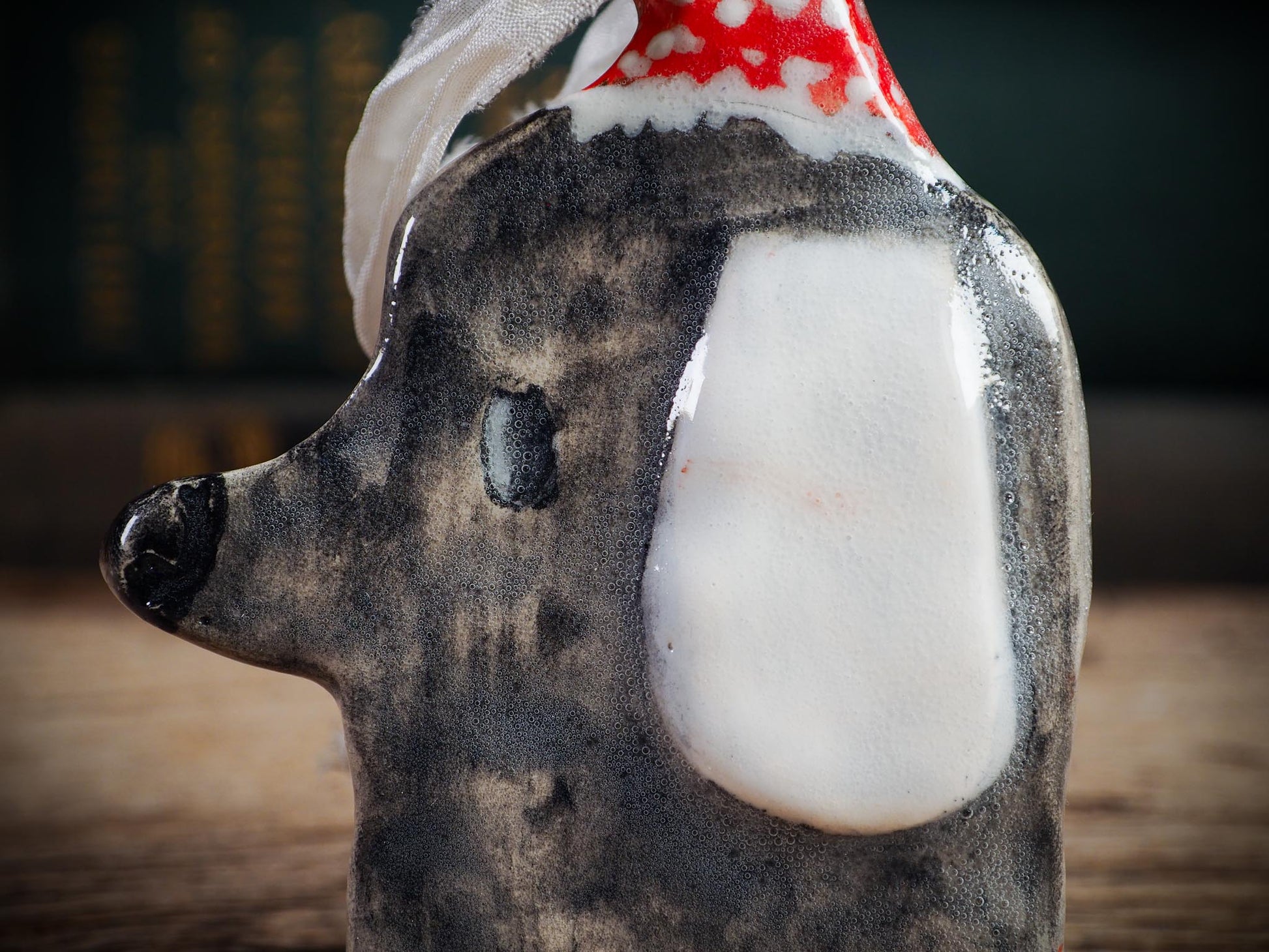 Handmade ceramic dog ornament with gray coat, white ear, and red dotted hood, created by Idania Salcido aka Danita Art for Christmas decorating or gifting.