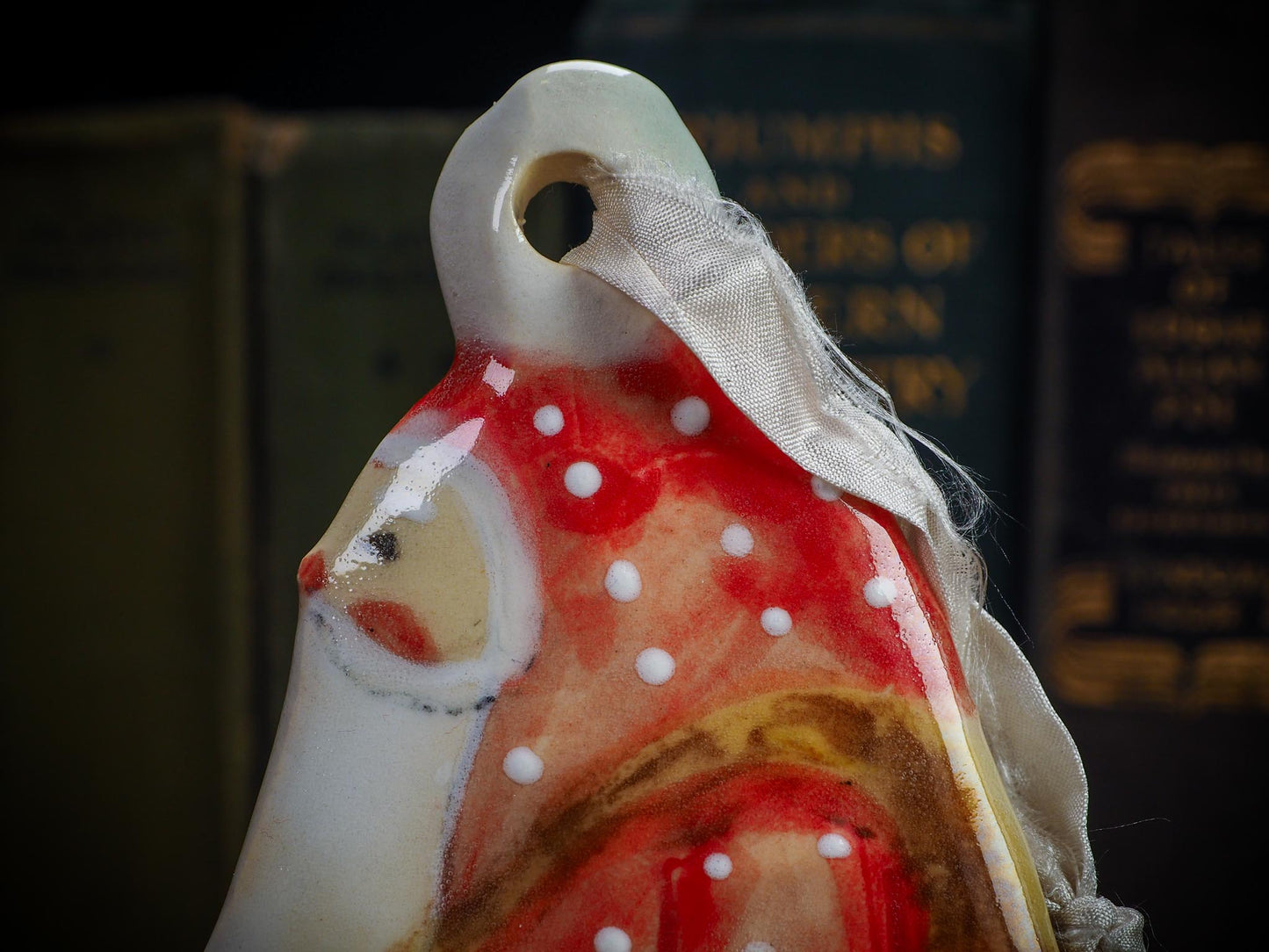 Handmade ceramic winter figure ornament with red dotted coat and ribbon, created by Idania Salcido AKA Danita Art for Christmas decorating or gifting.