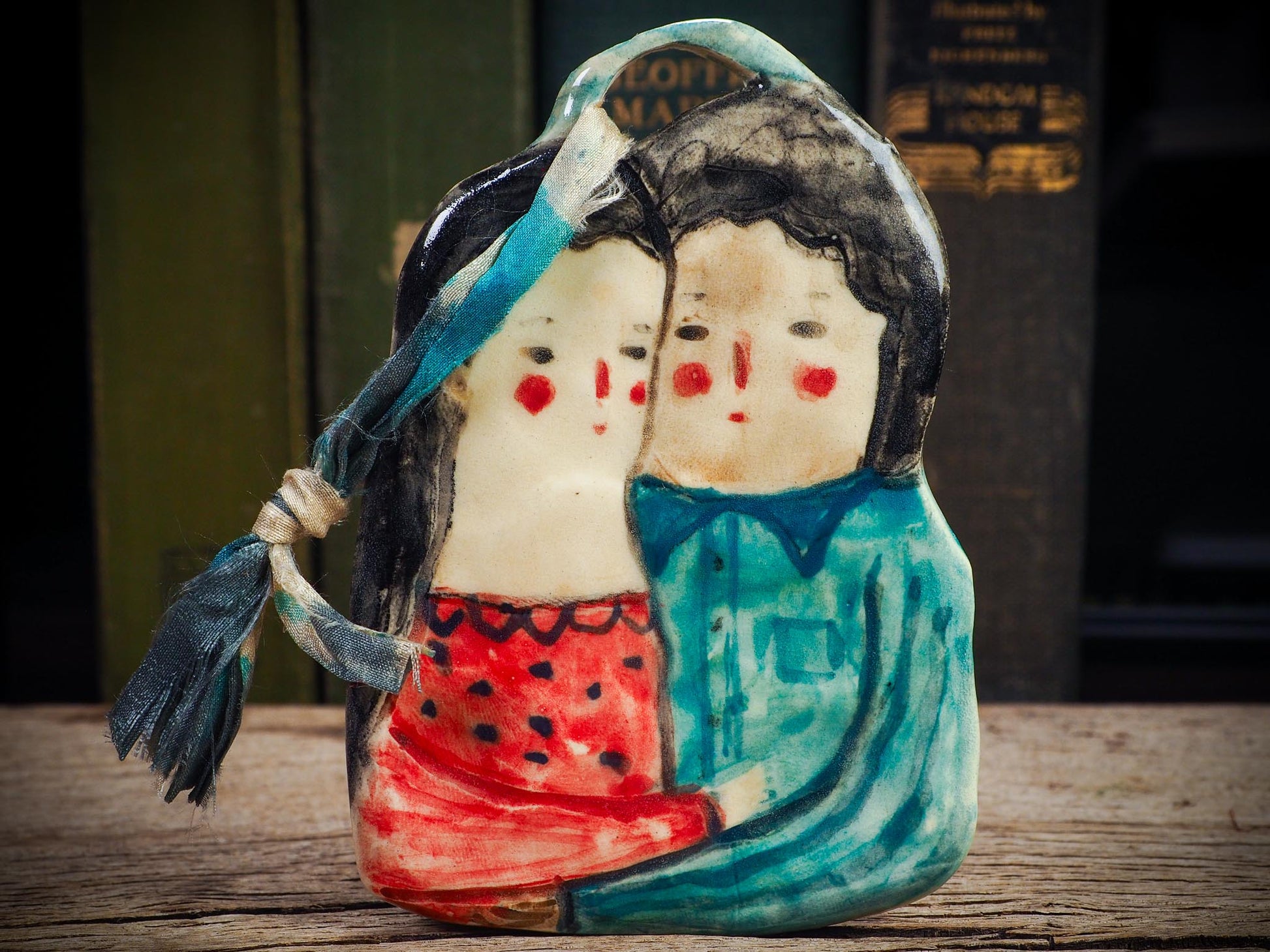 Handmade ceramic winter couple ornament with painted scarves and ribbon, created by Idania Salcido aka Danita Art for Christmas decoration or gifting.