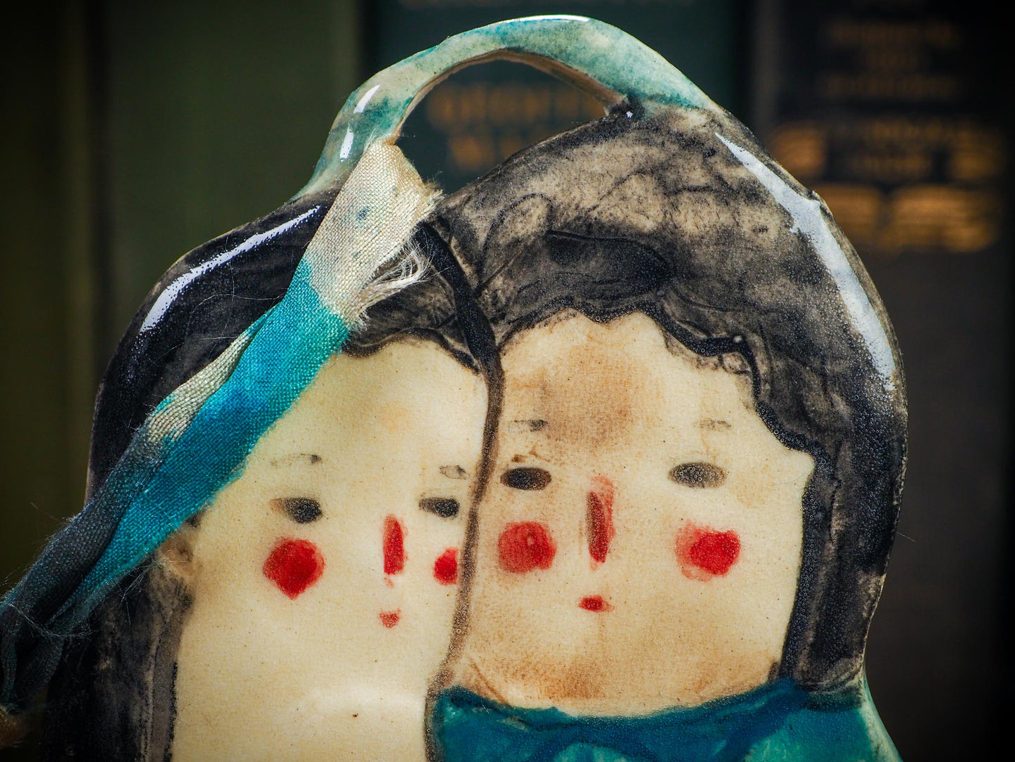 Handmade ceramic winter couple ornament with painted scarves and ribbon, created by Idania Salcido aka Danita Art for Christmas decoration or gifting.