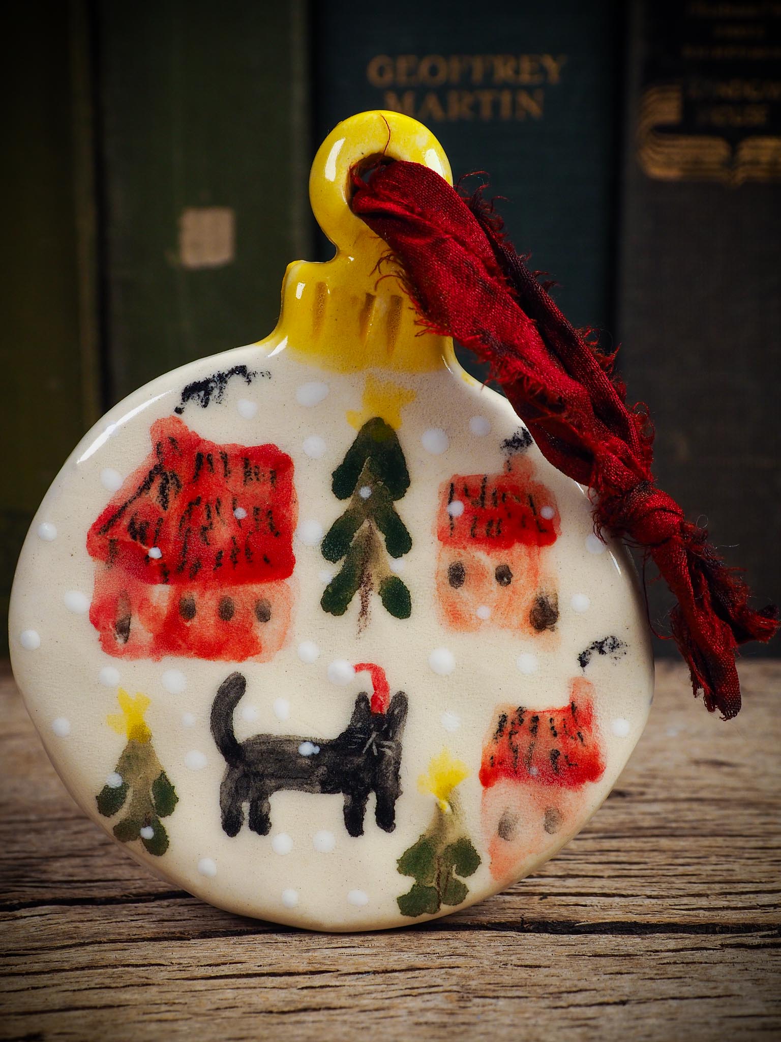 Handmade ceramic ornament of a black cat in a snowy village by Idania Salcido aka Danita Art.