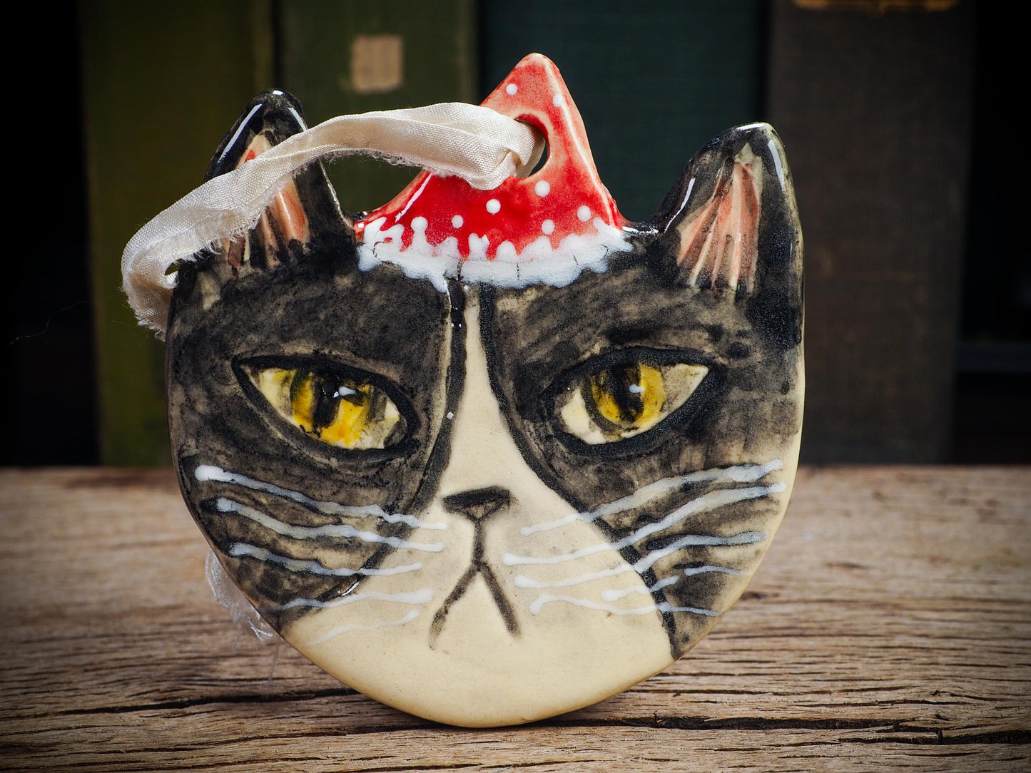 Handmade ceramic black and white tuxedo cat ornament with red holiday hat and ribbon, created by Idania Salcido Danita Art for Christmas decoration or gifting.