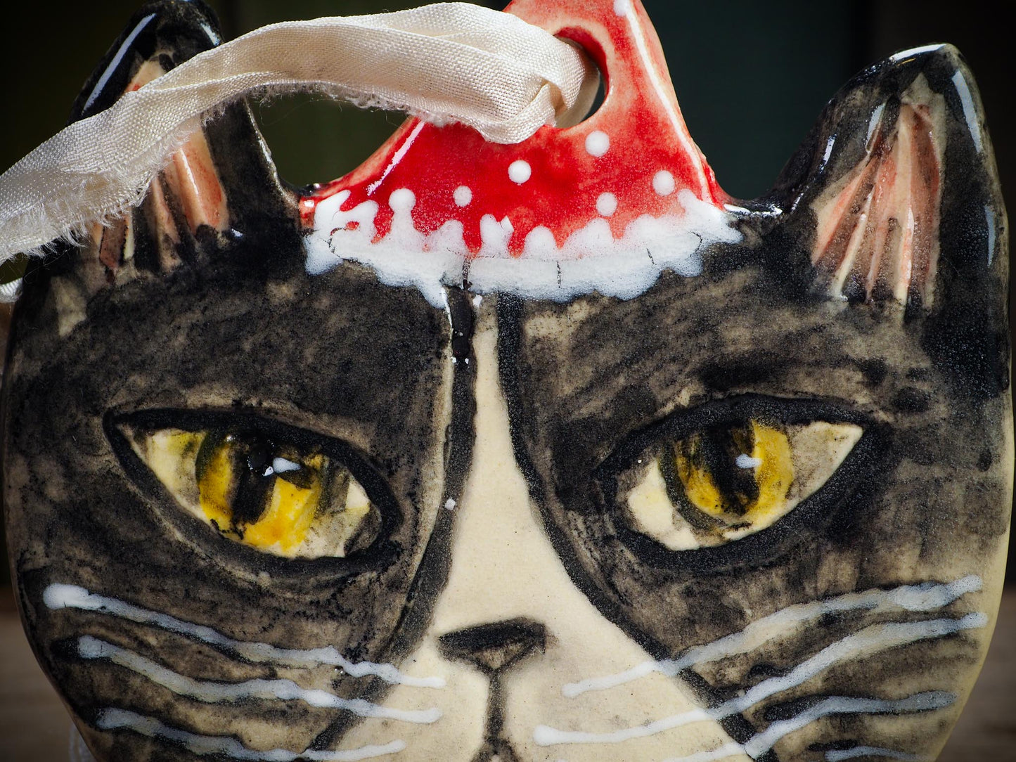 Handmade ceramic black and white tuxedo cat ornament with red holiday hat and ribbon, created by Idania Salcido Danita Art for Christmas decoration or gifting.