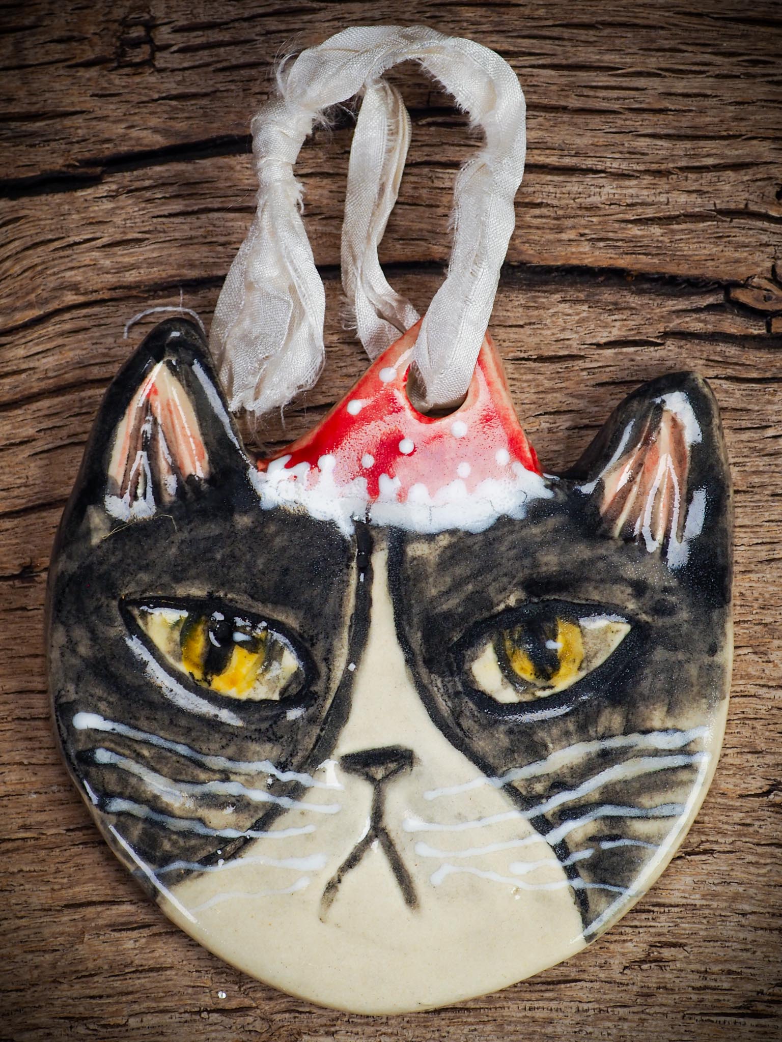 Handmade ceramic black and white tuxedo cat ornament with red holiday hat and ribbon, created by Idania Salcido Danita Art for Christmas decoration or gifting.