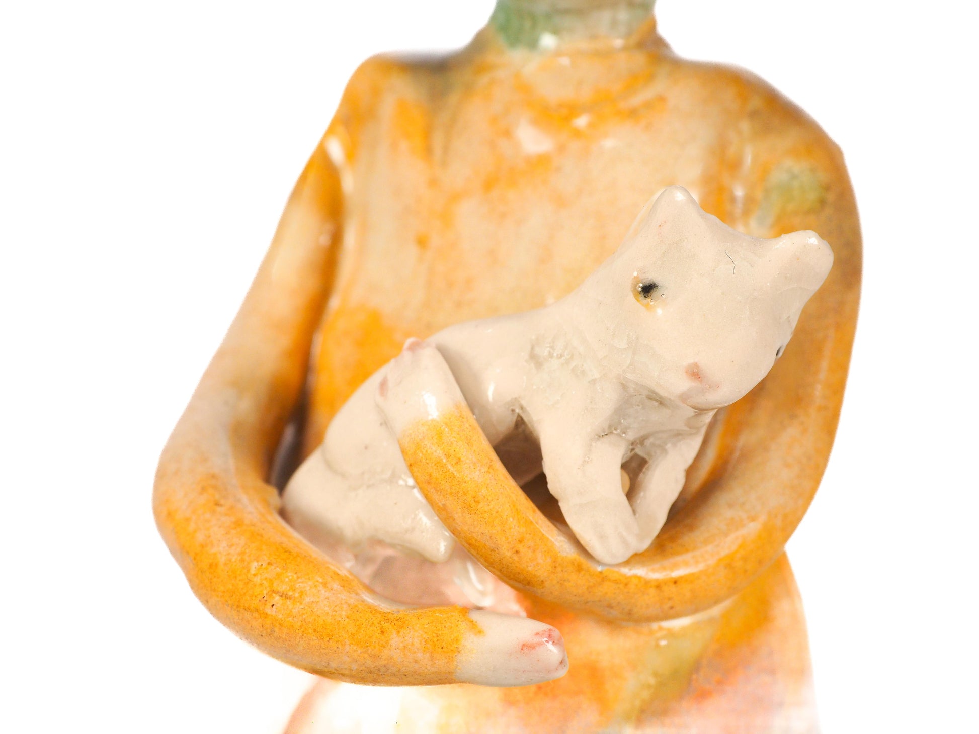 A ceramic figurine of a person in a yellow-orange robe holding a small cream-colored cat, By Idania Salcido (Danita Art).