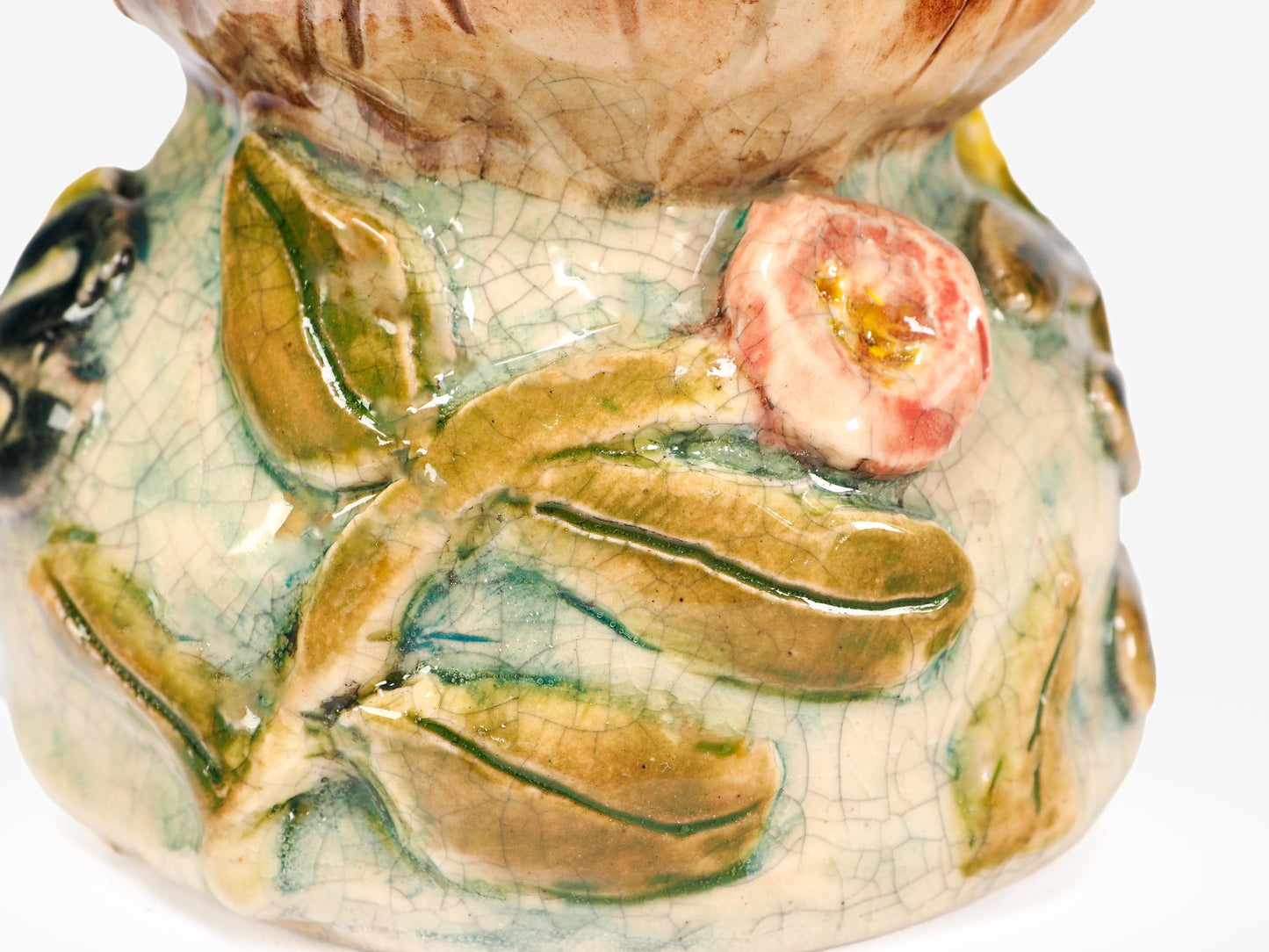 Close-up of a hand-painted ceramic pot with a glossy glaze, featuring green leaves, a pink rose, and a brown textured rim by Idania Salcido (Danita Art).