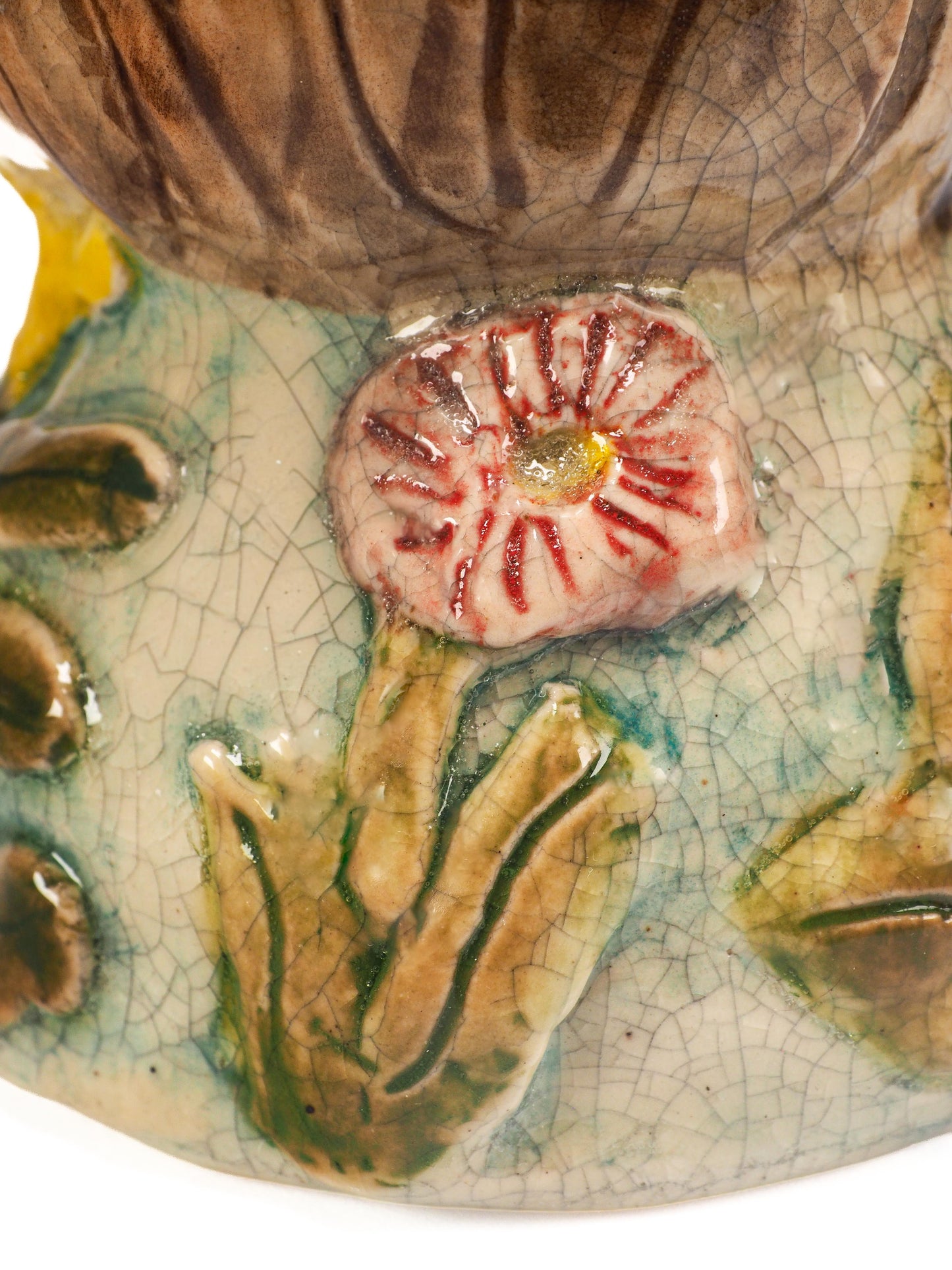 A close-up of a hand-painted ceramic figurine featuring a stylized face with green eyes, pink cheeks, brown hair, a yellow flower, and a green leafy body with a pink flower by Idania Salcido (Danita Art).