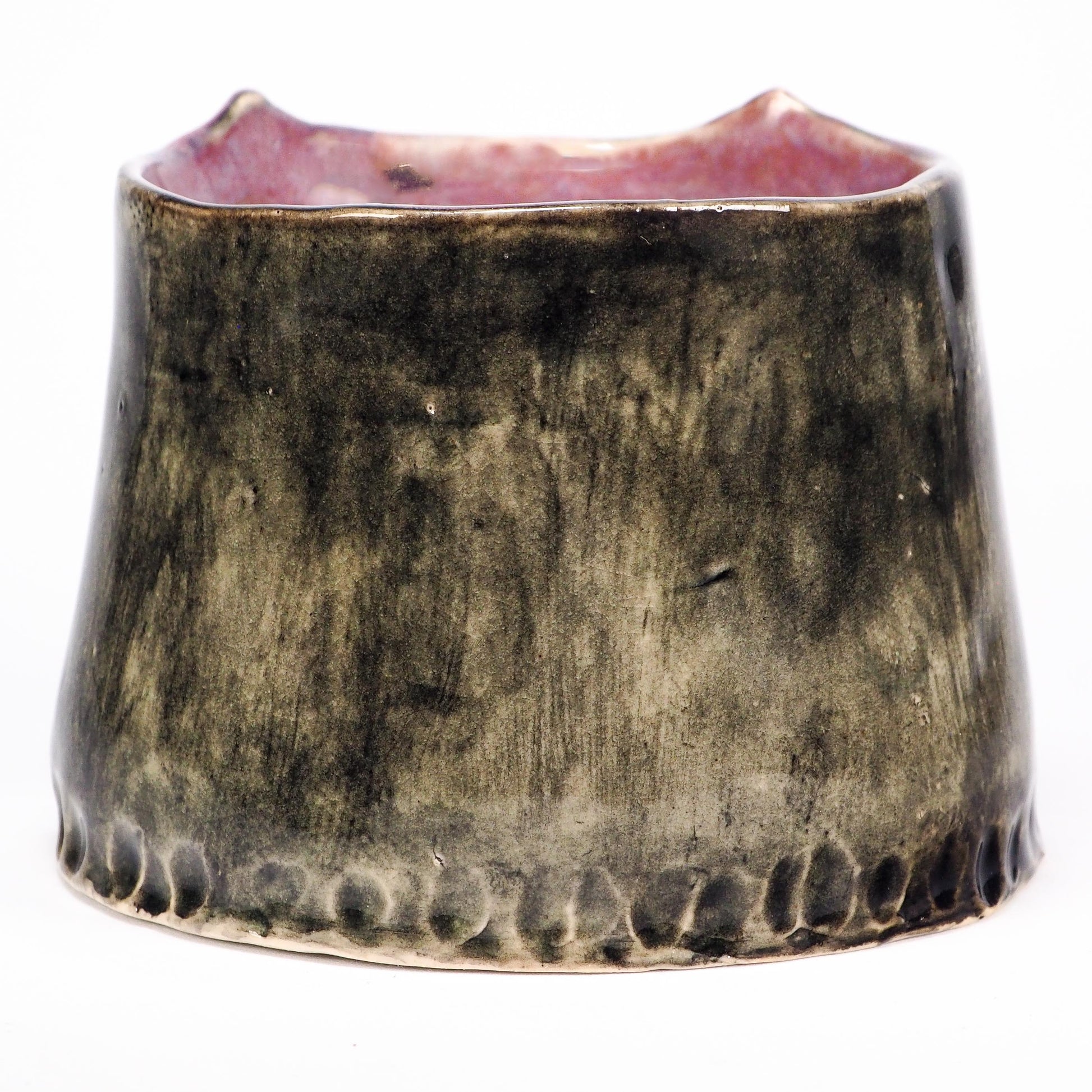 A handmade ceramic cup with a wide, flared shape, featuring a textured, mottled glaze in dark brown and black with a pinkish glaze visible on the inner rim by Idania Salcido (Danita Art).