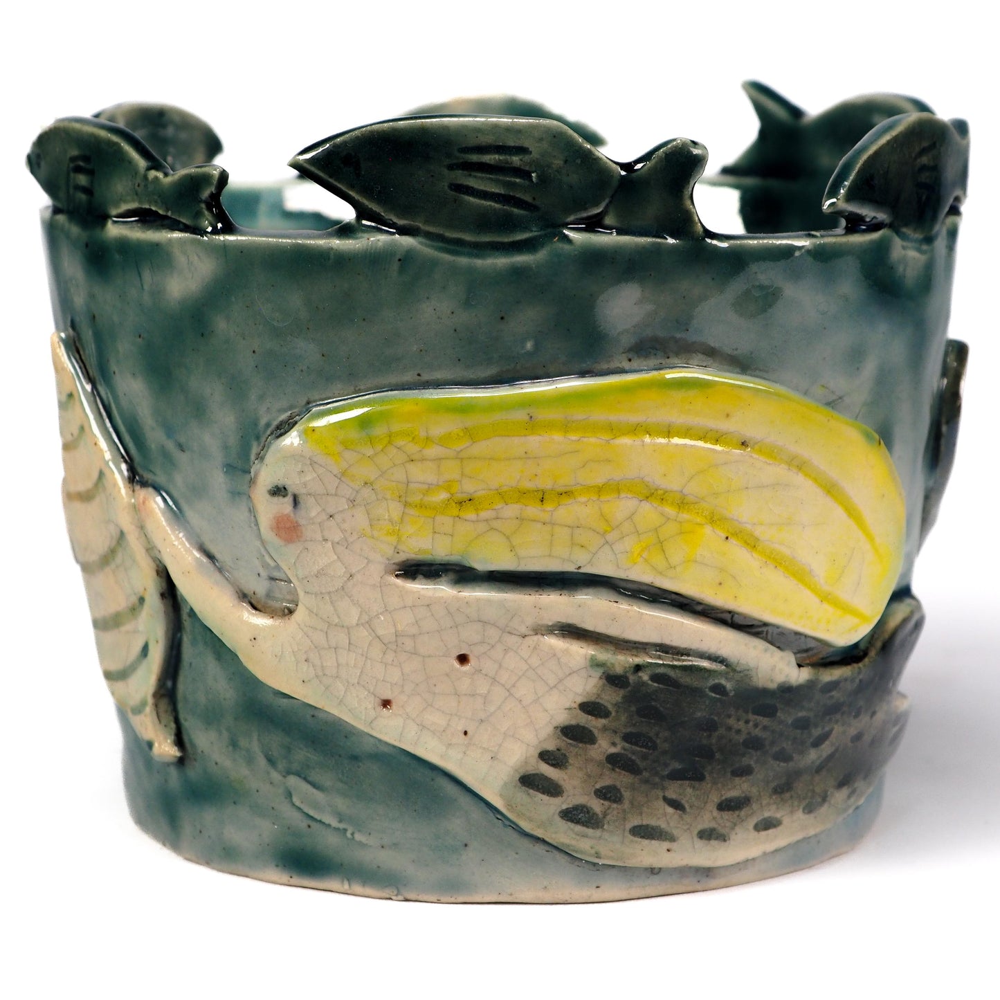 A handmade ceramic vase featuring a stylized fish design with a glossy yellow and cream body, set against a textured dark green glazed background with small fish figures along the top edge by Idania Salcido (Danita Art)