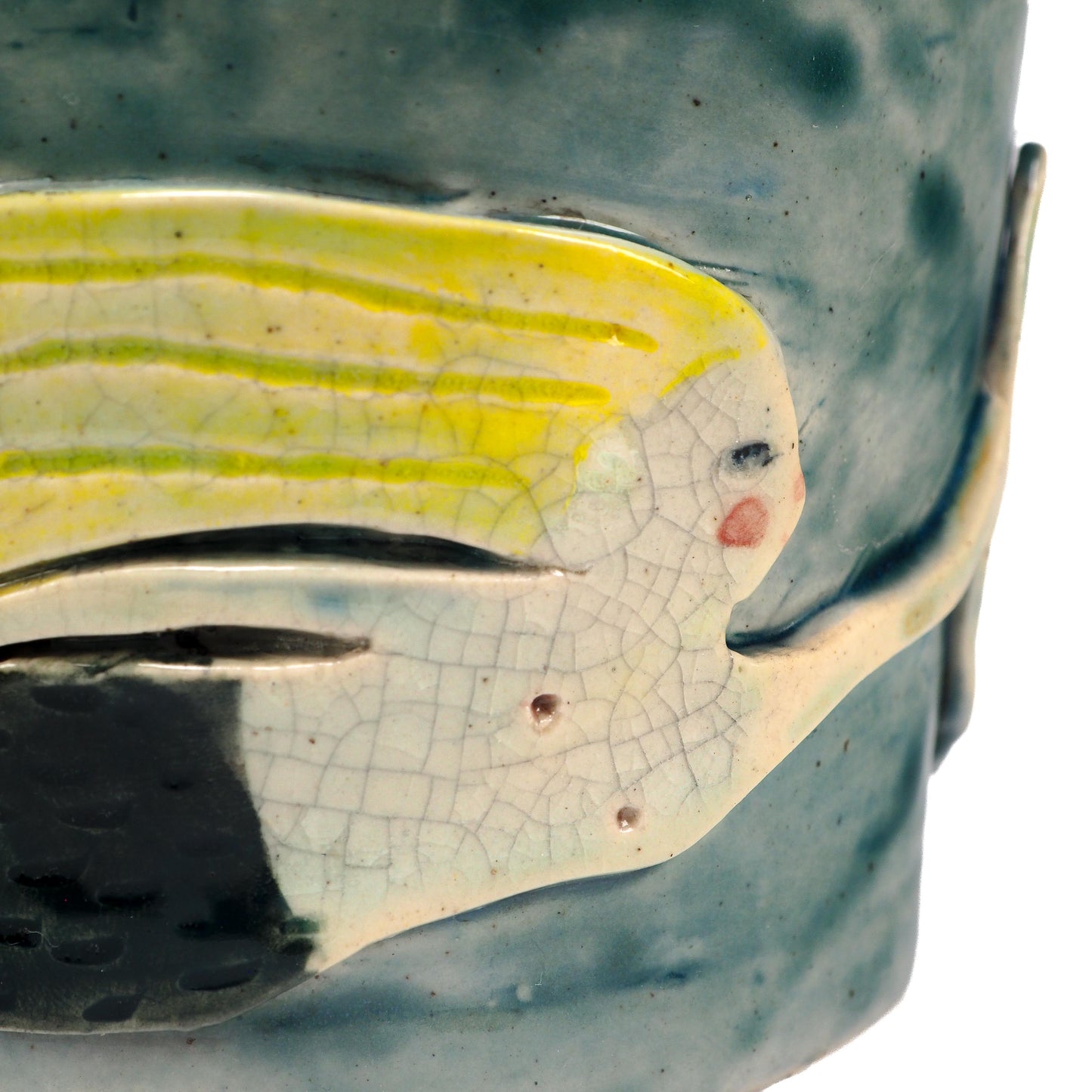 Close-up of a ceramic fish-shaped decorative piece mounted on a textured blue-green cylindrical base, featuring a pale yellow and off-white fish with crackled glaze details by Idania Salcido (Danita Art).
