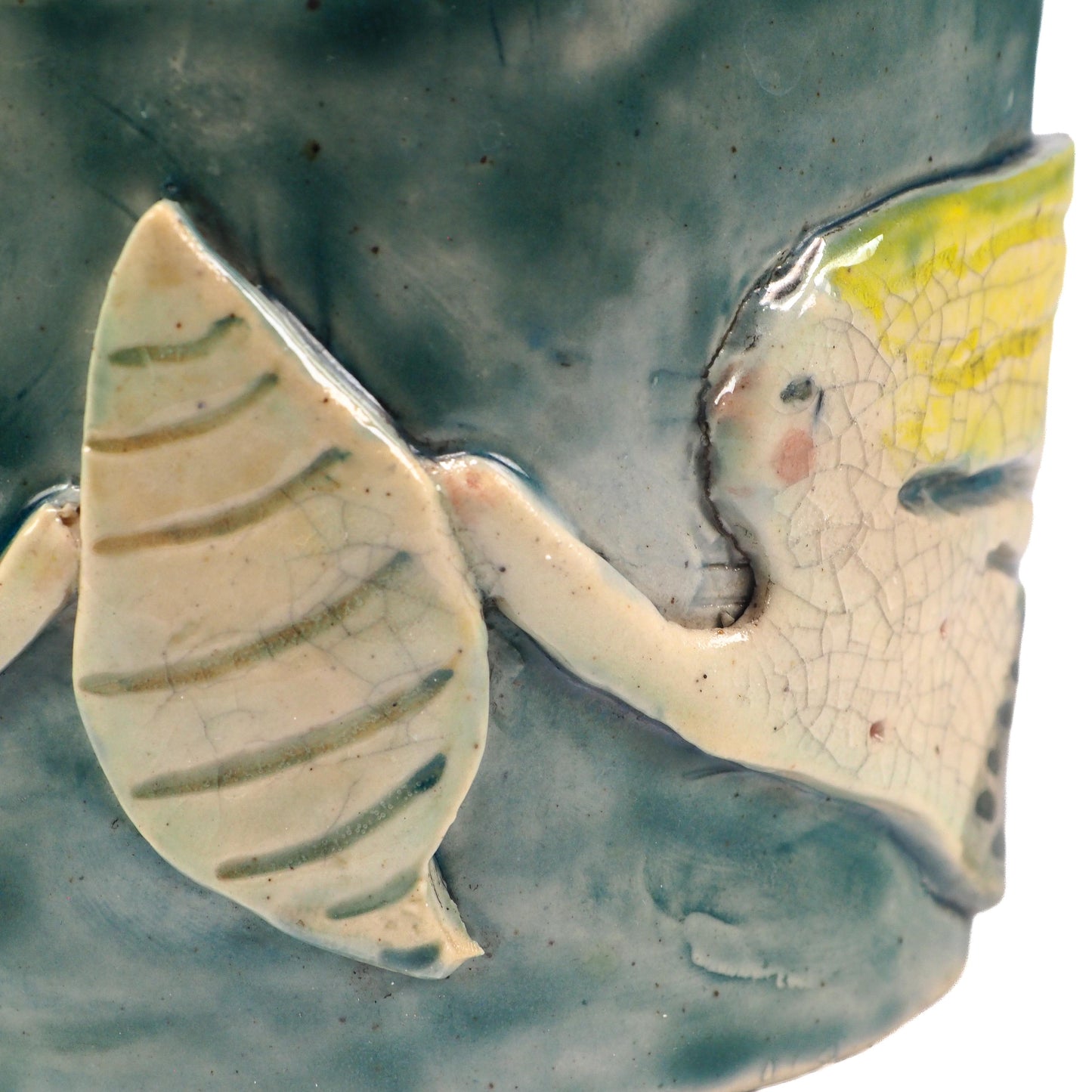 Close-up of a ceramic fish-shaped decorative piece mounted on a textured blue-green cylindrical base, featuring a pale yellow and off-white fish with crackled glaze details by Idania Salcido (Danita Art).