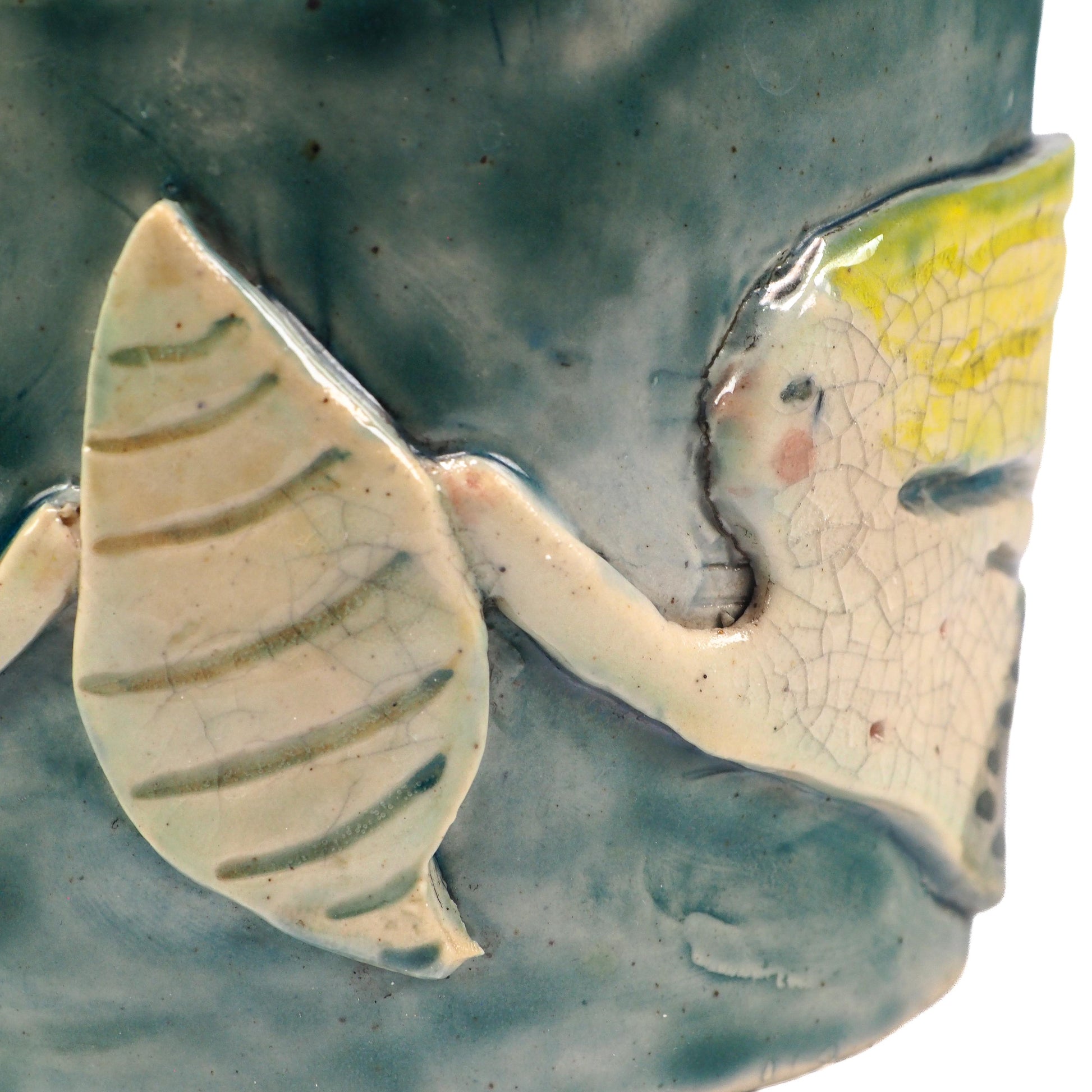 Close-up of a ceramic fish-shaped decorative piece mounted on a textured blue-green cylindrical base, featuring a pale yellow and off-white fish with crackled glaze details by Idania Salcido (Danita Art).