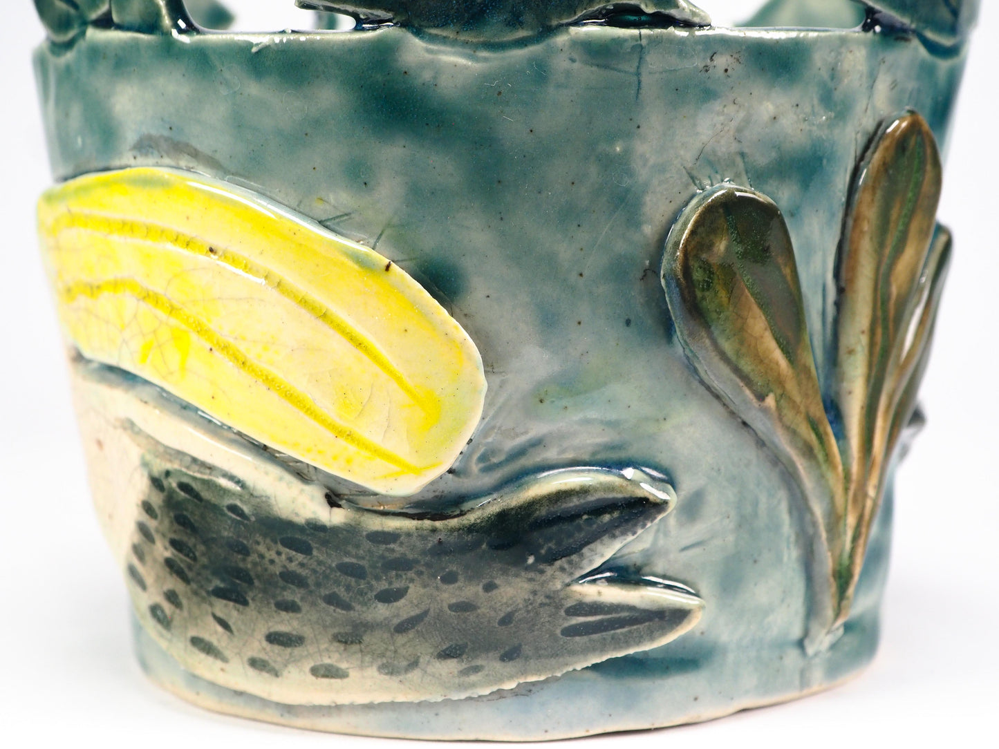 Close-up of a ceramic fish-shaped decorative piece mounted on a textured blue-green cylindrical base, featuring a pale yellow and off-white fish with crackled glaze details by Idania Salcido (Danita Art).