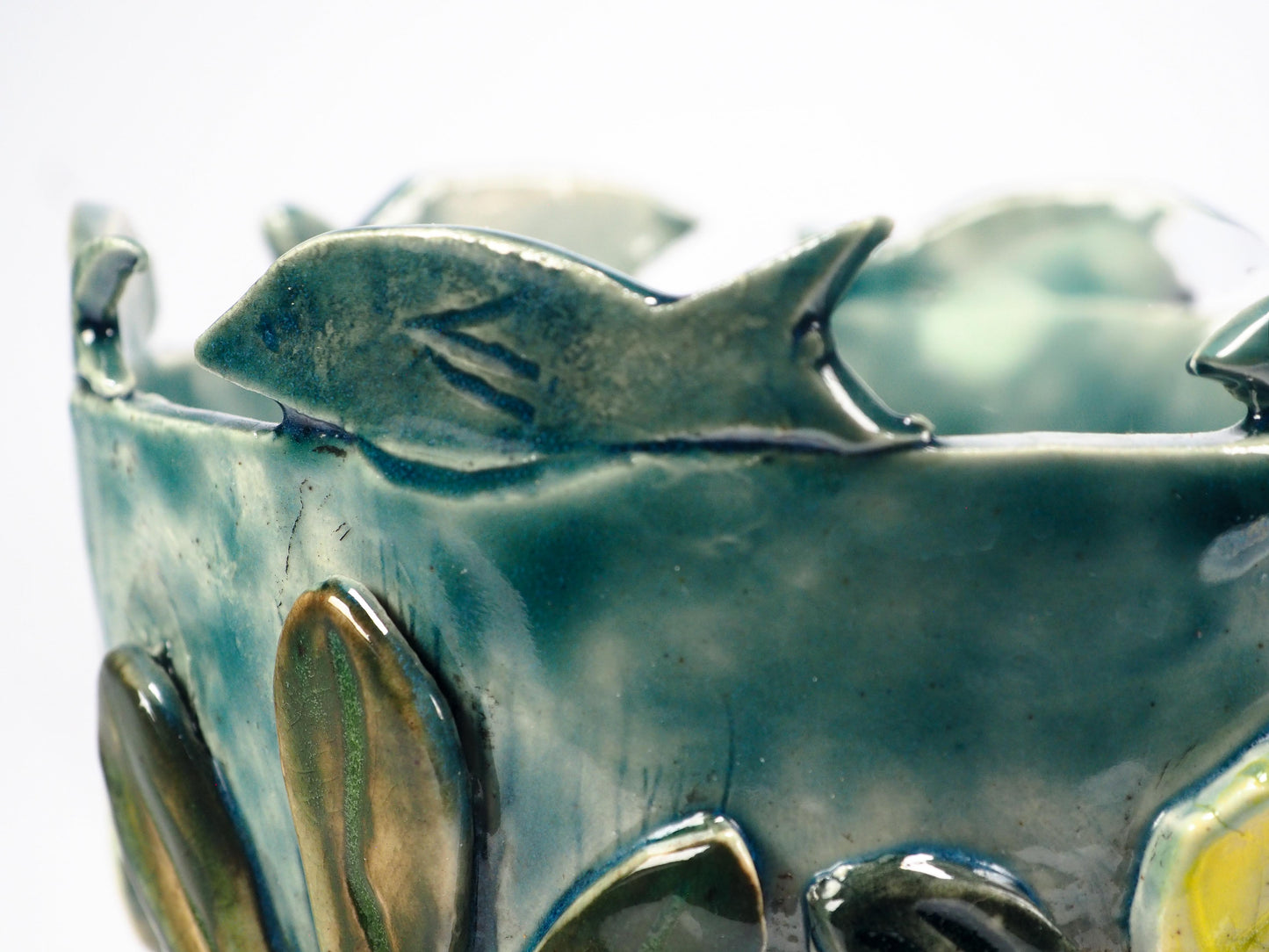 Close-up of a ceramic fish-shaped decorative piece mounted on a textured blue-green cylindrical base, featuring a pale yellow and off-white fish with crackled glaze details by Idania Salcido (Danita Art).