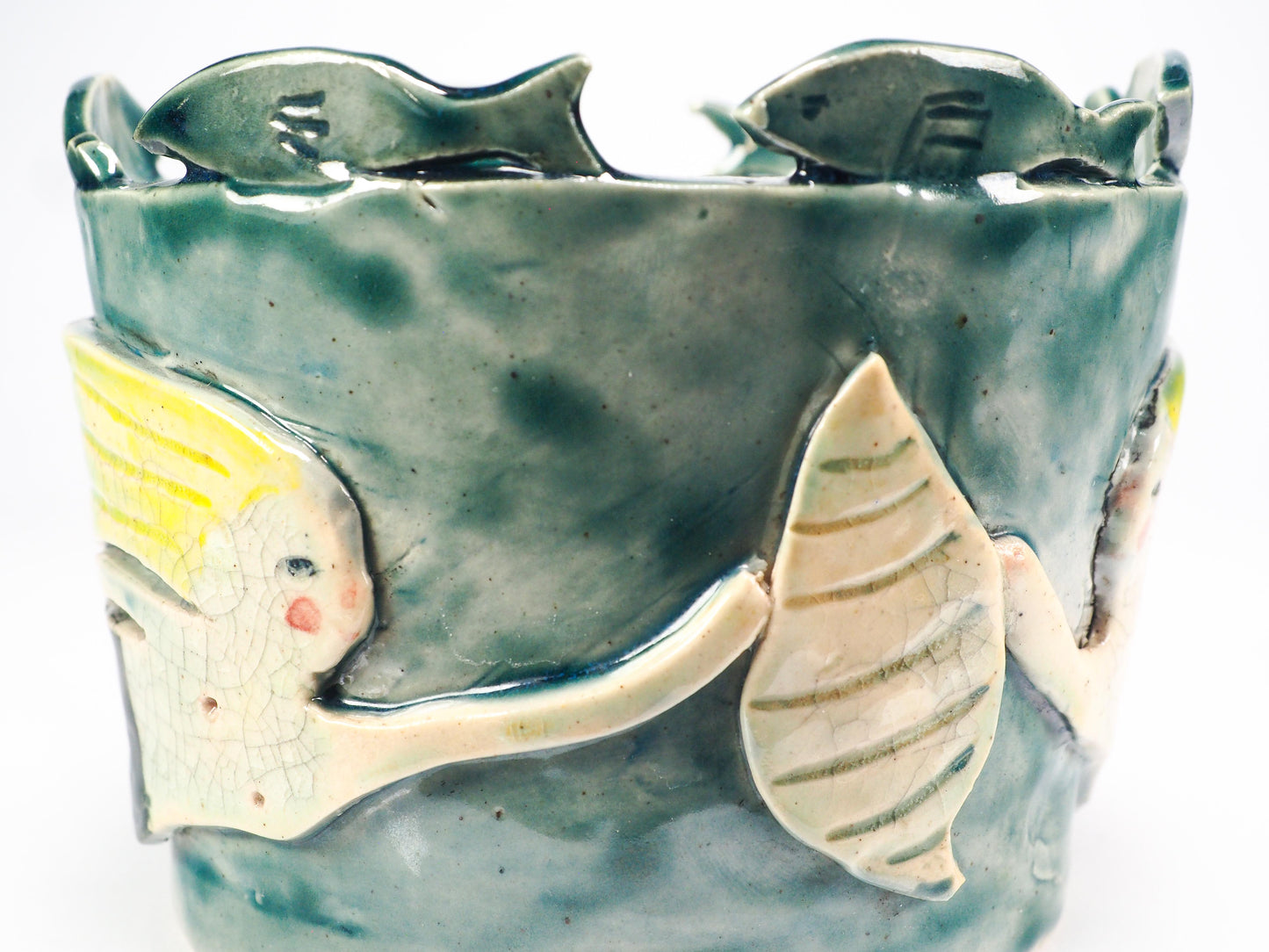 Close-up of a ceramic fish-shaped decorative piece mounted on a textured blue-green cylindrical base, featuring a pale yellow and off-white fish with crackled glaze details by Idania Salcido (Danita Art).