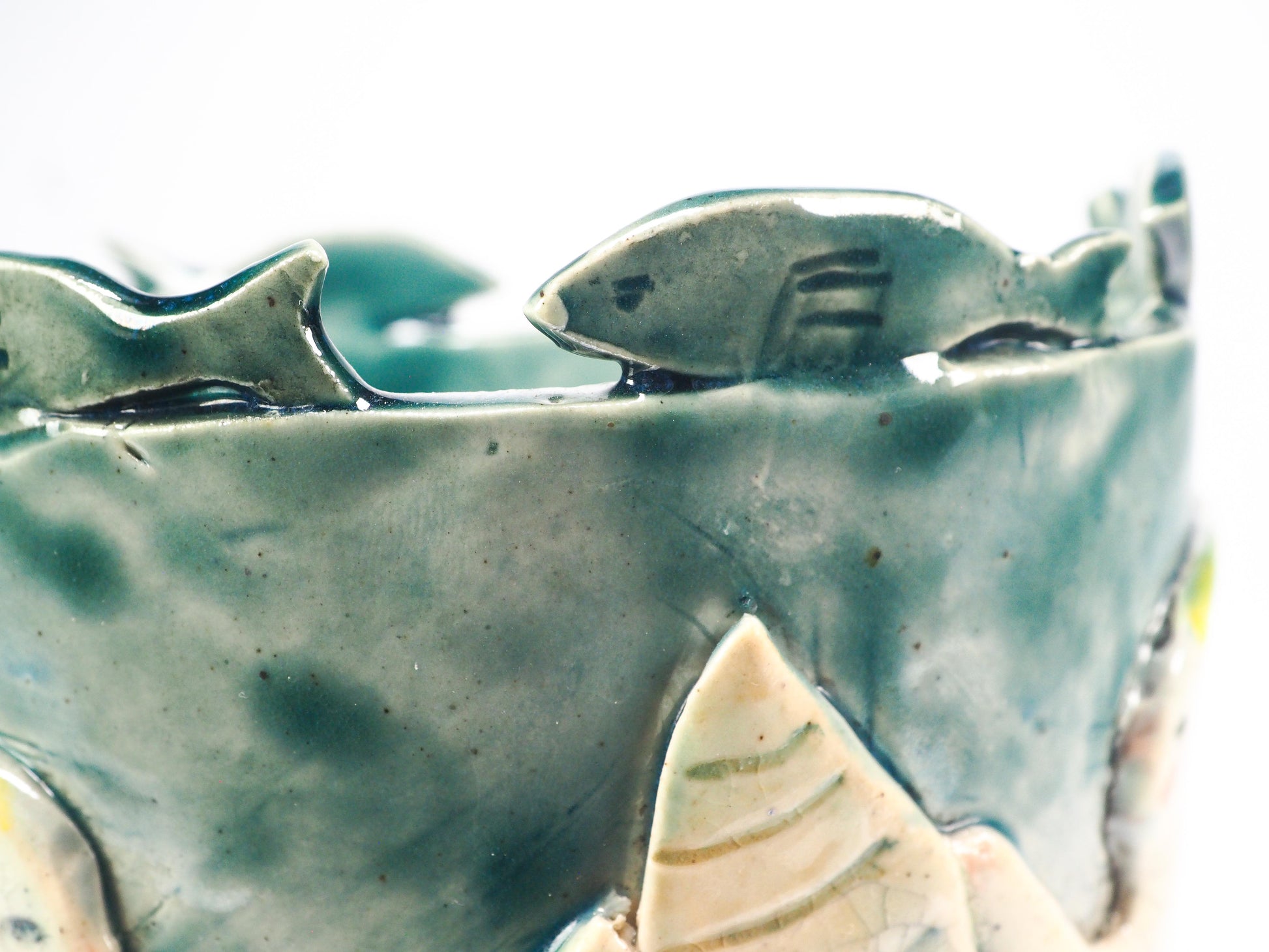 Close-up of a ceramic fish-shaped decorative piece mounted on a textured blue-green cylindrical base, featuring a pale yellow and off-white fish with crackled glaze details by Idania Salcido (Danita Art).