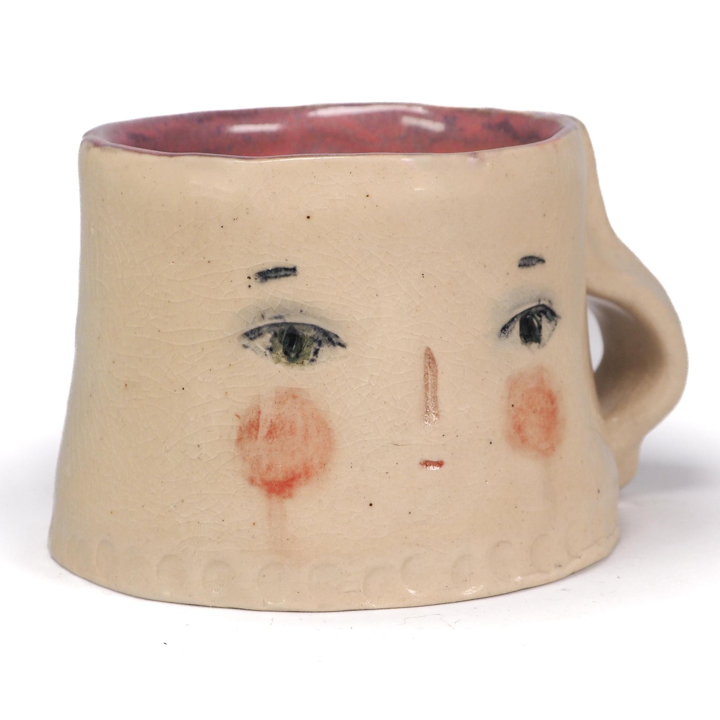 A handmade ceramic mug with a face design, featuring a beige stoneware body, hand-painted black eyes and eyebrows, pinkish-red cheeks, and a reddish-brown interior by Idania Salcido (Danita Art).
