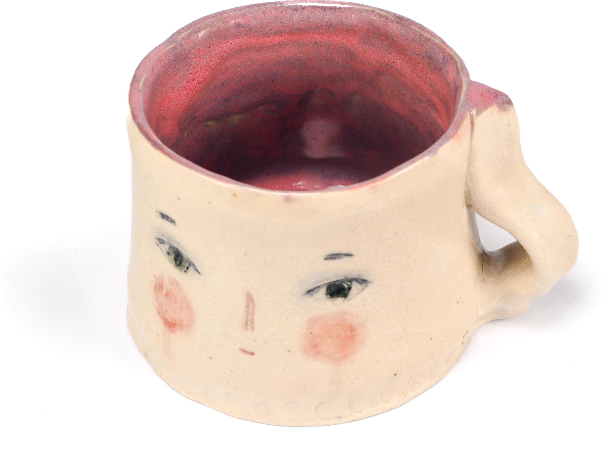 A handmade ceramic mug with a handle, featuring a hand-painted face on the front with green eyes, a small nose, and pink cheeks by Idania Salcido (Danita Art).