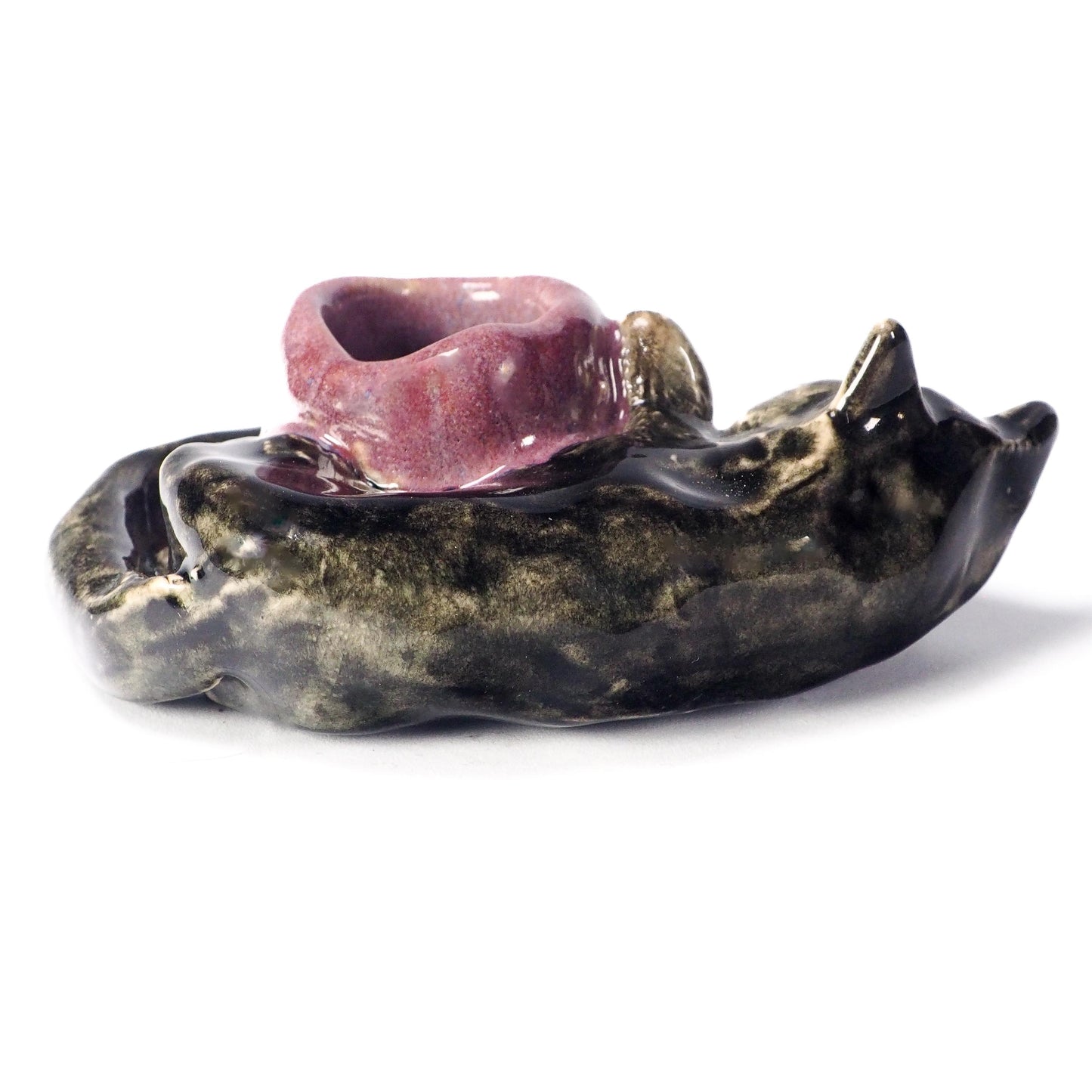 A ceramic sculptural candle holder shaped like a sleeping cat, featuring a glossy black and gold marbled body with a contrasting pinkish-purple glazed bowl on top by Idania Salcido (Danita Art).
