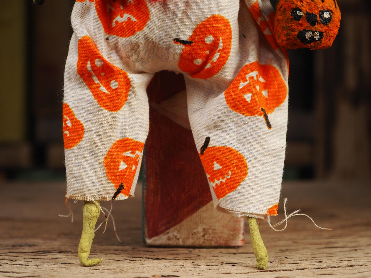 A close-up of a handmade rag doll's lower body wearing cream-colored pants with orange pumpkin prints, holding an orange pumpkin head, standing on a wooden surface.
An original spooky cute outsider folk art Halloween Doll. Hand made using spun cotton, paper and fabric to create the perfect Halloween ornament for your tree. Specially created for someone who appreciates fine and unique art gifts, It is a one of a kind original design by Idania Salcido (Danita Art).