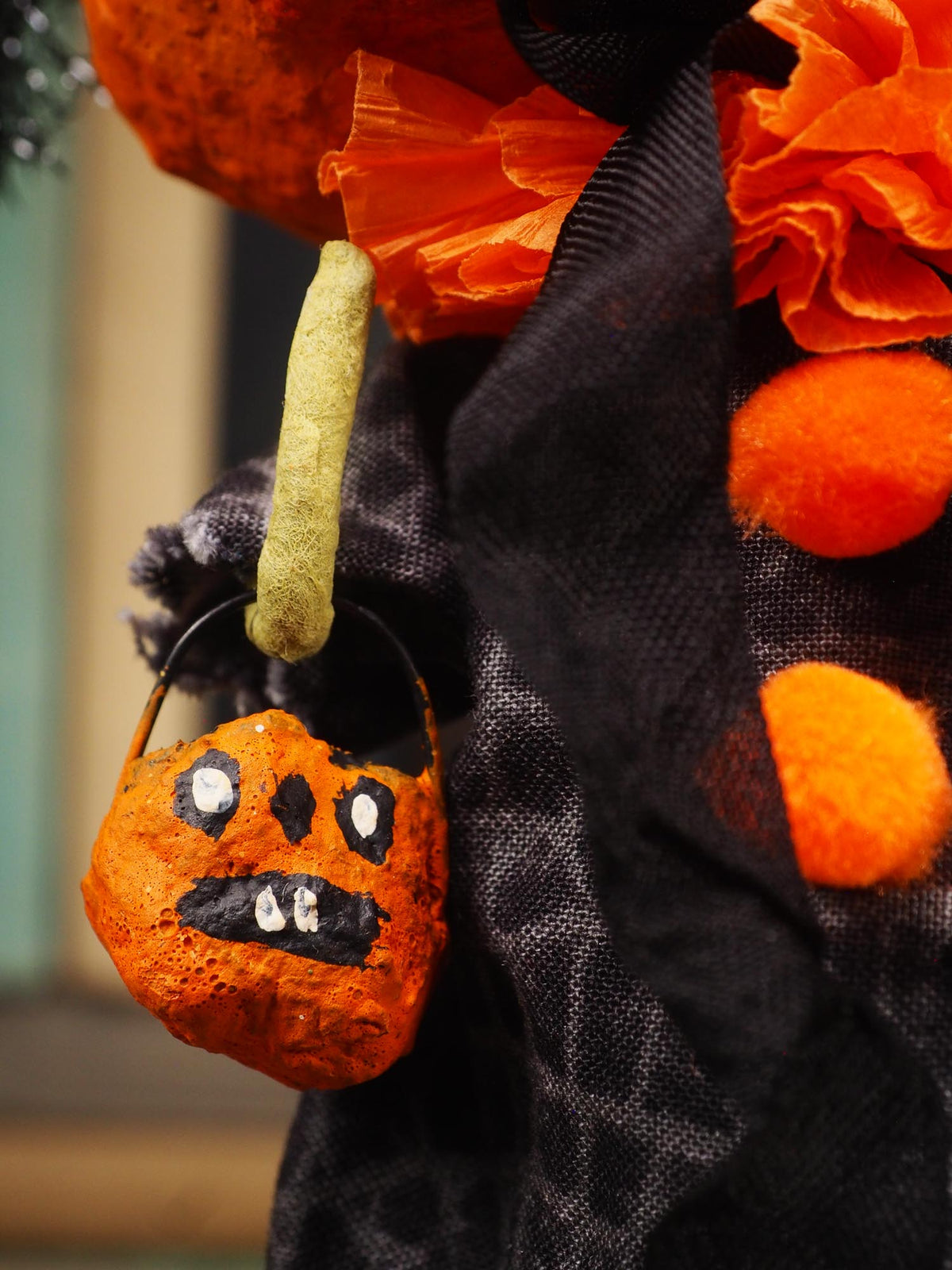 Close-up of a Halloween decoration featuring a small orange pumpkin bucket with a painted spooky face hanging from a black fabric garland with orange pom-poms and tissue paper.
An original spooky cute folk outsider art Halloween Doll. Hand made using spun cotton, paper and fabric to create the perfect Halloween ornament for your tree. Specially created for someone who appreciates fine and unique art gifts, It is a one of a kind original design by Idania Salcido (Danita Art).