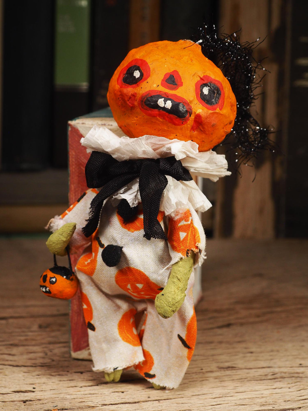 A handmade Halloween doll with a carved orange pumpkin head, black tinsel hair, a black ribbon bow, and an orange-and-white patterned dress, posed on a wooden surface.
An original handmade spun cotton Halloween art doll by Idania Salcido (Danita Art).