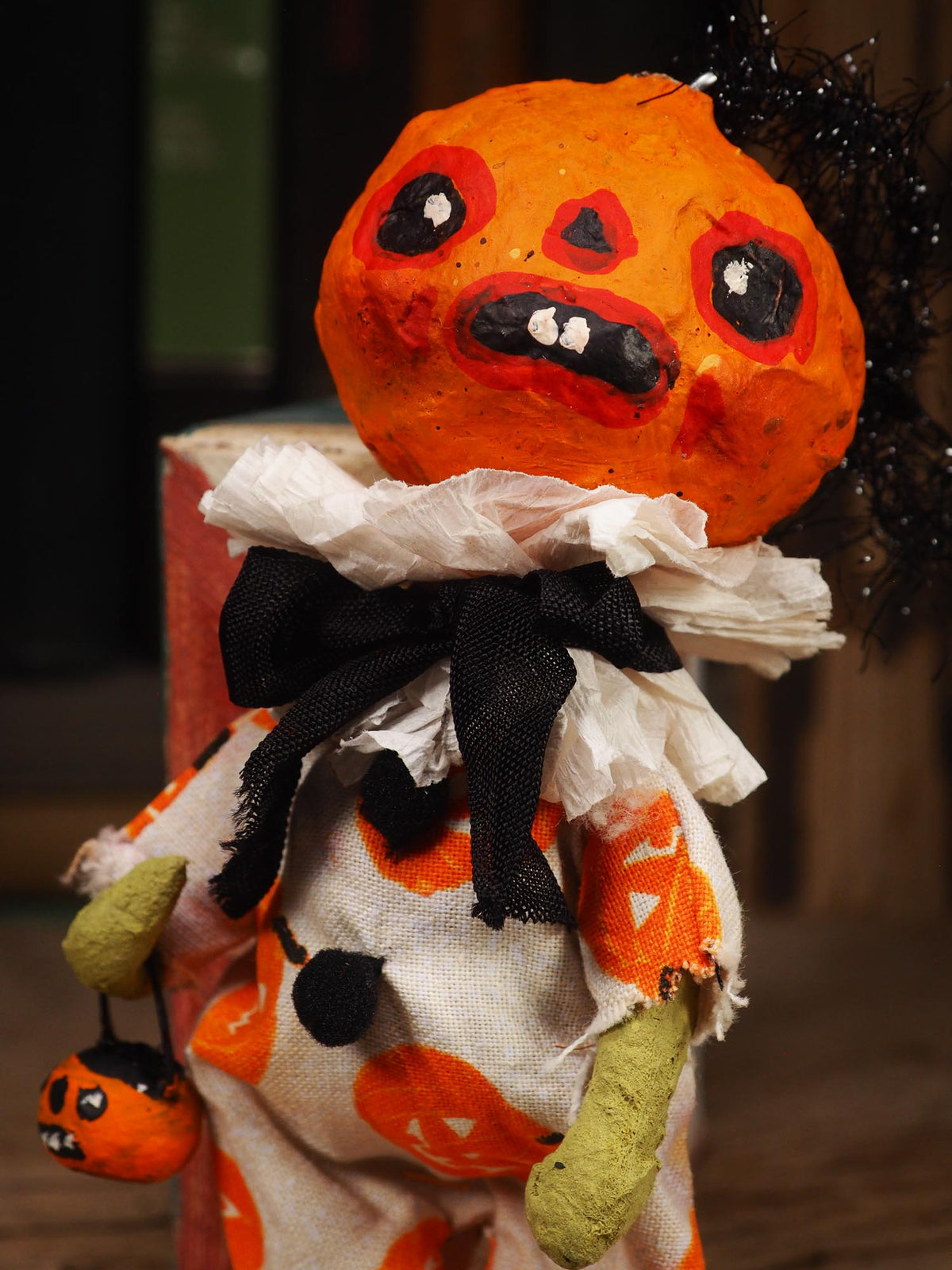 A handmade Halloween doll with a large orange pumpkin head, black tinsel hair, a black ribbon bow, and a white ruffled collar, wearing a white dress with orange pumpkin prints.
An original handmade spun cotton Halloween art doll by Idania Salcido (Danita Art).