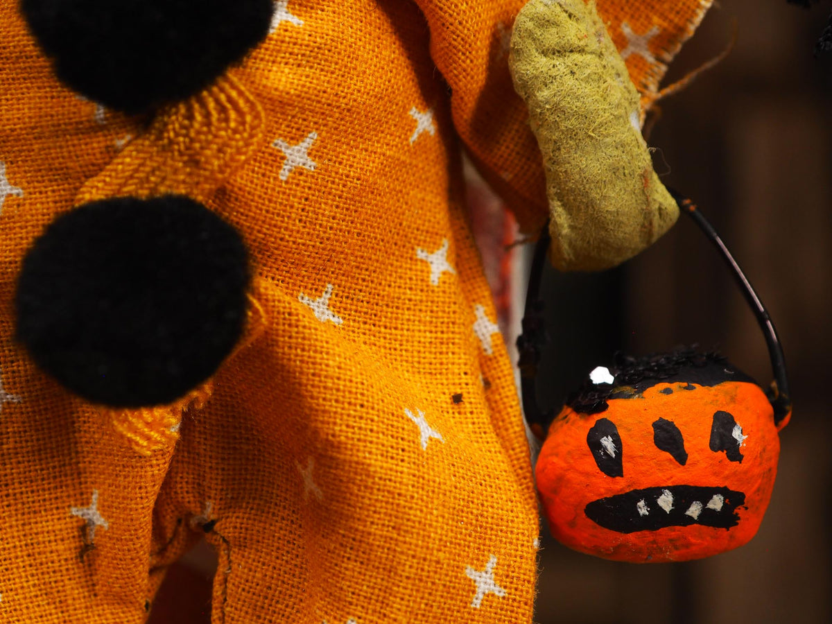 Close-up of an orange costume or fabric garment with black pom-poms, white star details, and a small orange jack-o'-lantern bucket with a black handle.
Original spun cotton hand made Halloween doll ornament by Idania Salcido (Danita Art)