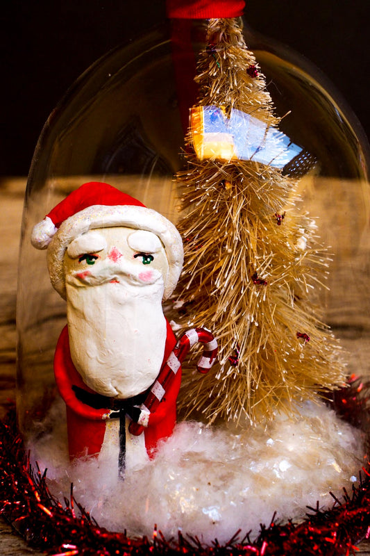 An original handmade christmas tree ornament by Idania Salcido. A clear domed diorama with a holiday scene with Santa Claus elves, Christmas Trees, Elves, Gifts and magical glitter deer. Perfect to decorate your Christmas Tree, your mantelpiece or to be used as accents on a dinner table.